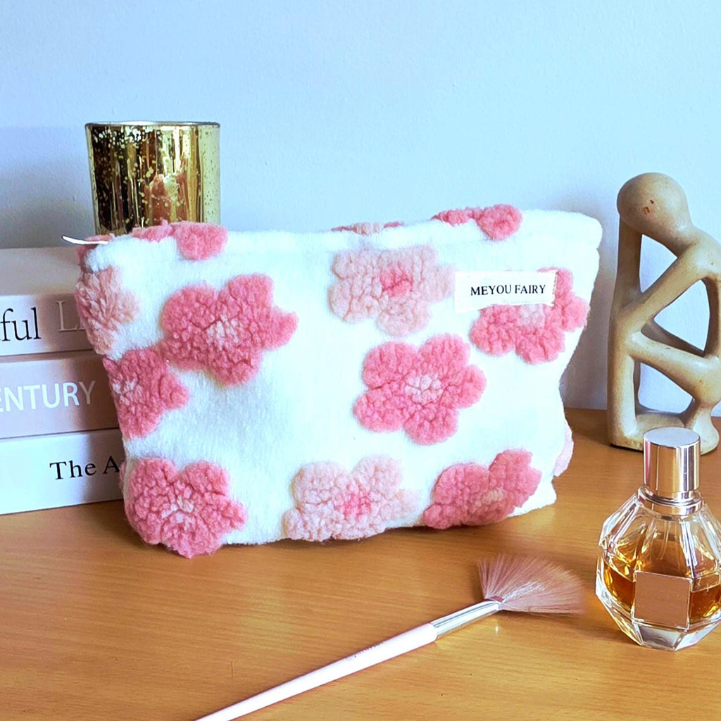 A white cosmetic bag with pink flower appliqués. The bag has a fluffy texture and a zipper closure. The label on the bag reads "MEYOU FAIRY".