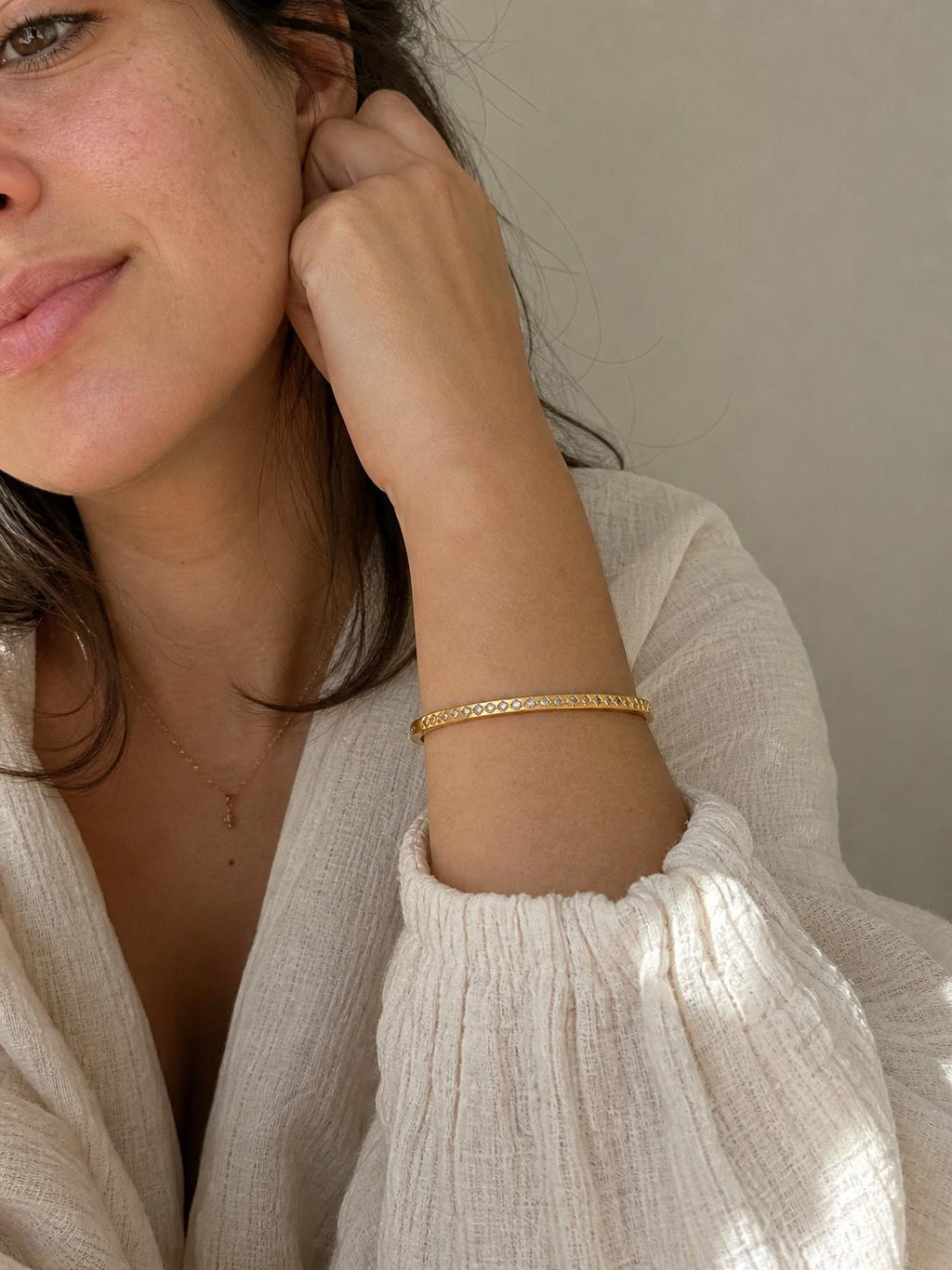 Gold-colored bangle bracelet with a repeating geometric pattern. The bracelet is worn on a person's arm, and the image is taken in natural light. The bracelet is a simple, elegant piece of jewelry.