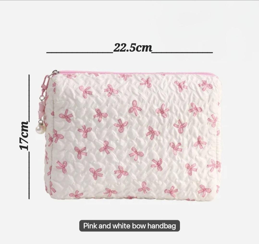 Image  includes A white quilted handbag with pink bow accents. The bag is rectangular, measuring 22.5 cm wide and 17 cm high. It has a pink zipper and trim. The text "Pink and white bow handbag" is at the bottom.