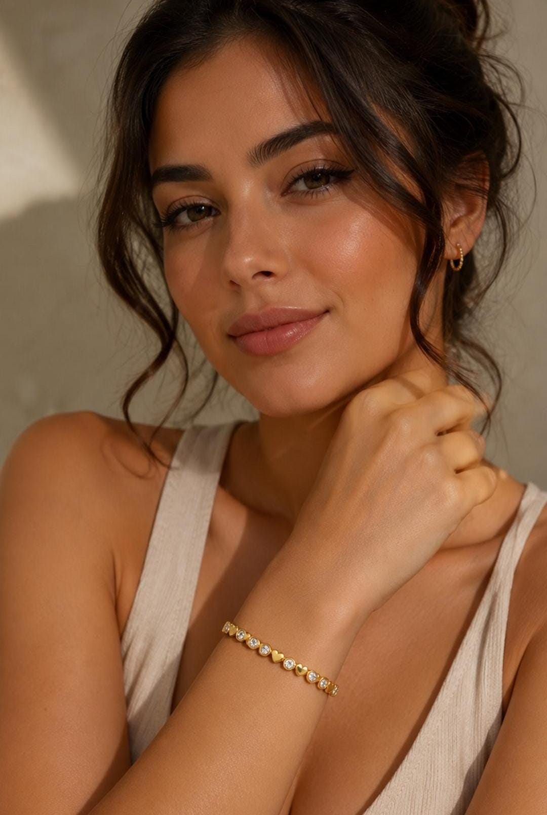 A gold-toned bracelet featuring a repeating pattern of circular clear stones set in metal bezels alternating with small, solid gold-toned heart shapes. The jewelry piece is worn on the wrist, showcasing a delicate and polished metallic finish.