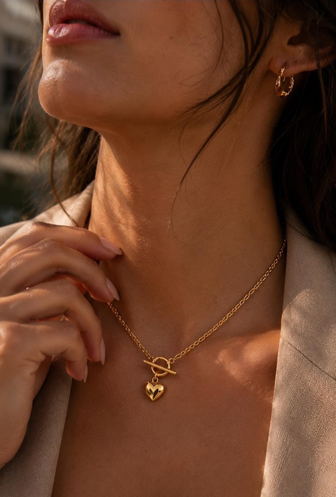 A gold-toned necklace featuring a delicate chain with a toggle clasp closure and a small, smooth, polished heart-shaped pendant hanging from the center. The metal has a reflective, warm yellow finish that catches the light.