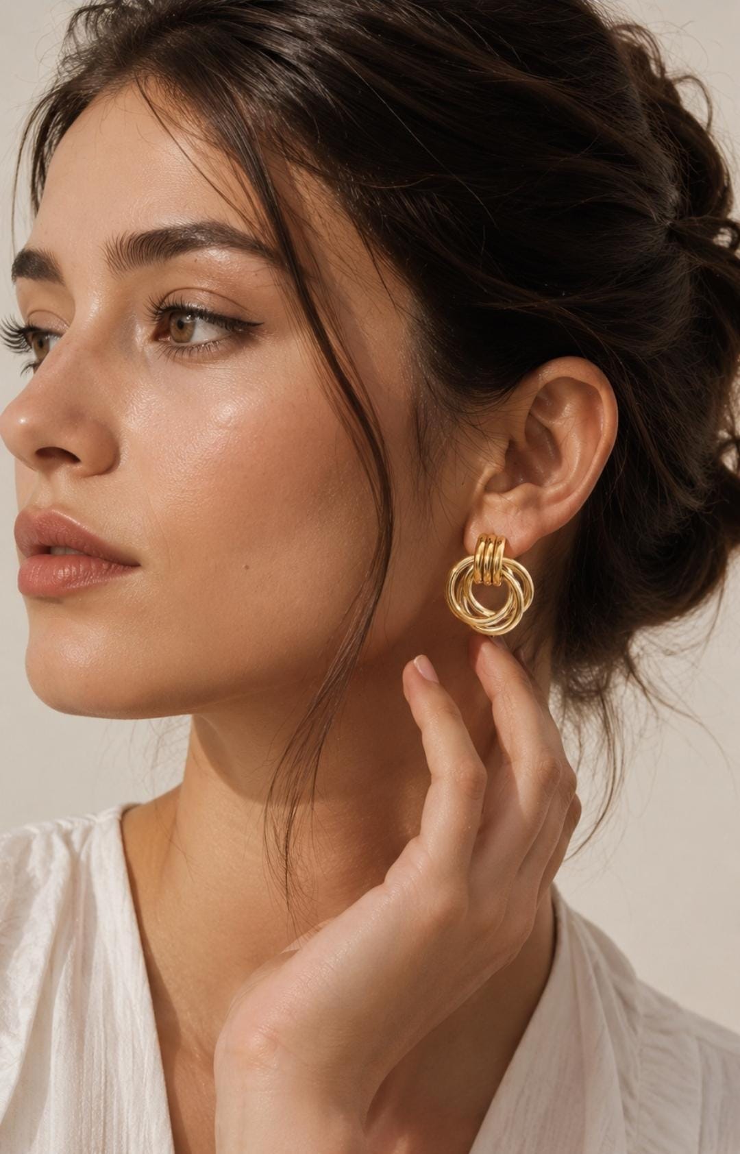 A gold-toned earring featuring a design of three interlocking circular rings suspended from a small, solid top loop. The metal has a polished, reflective finish, creating a bright, metallic appearance against the earlobe.