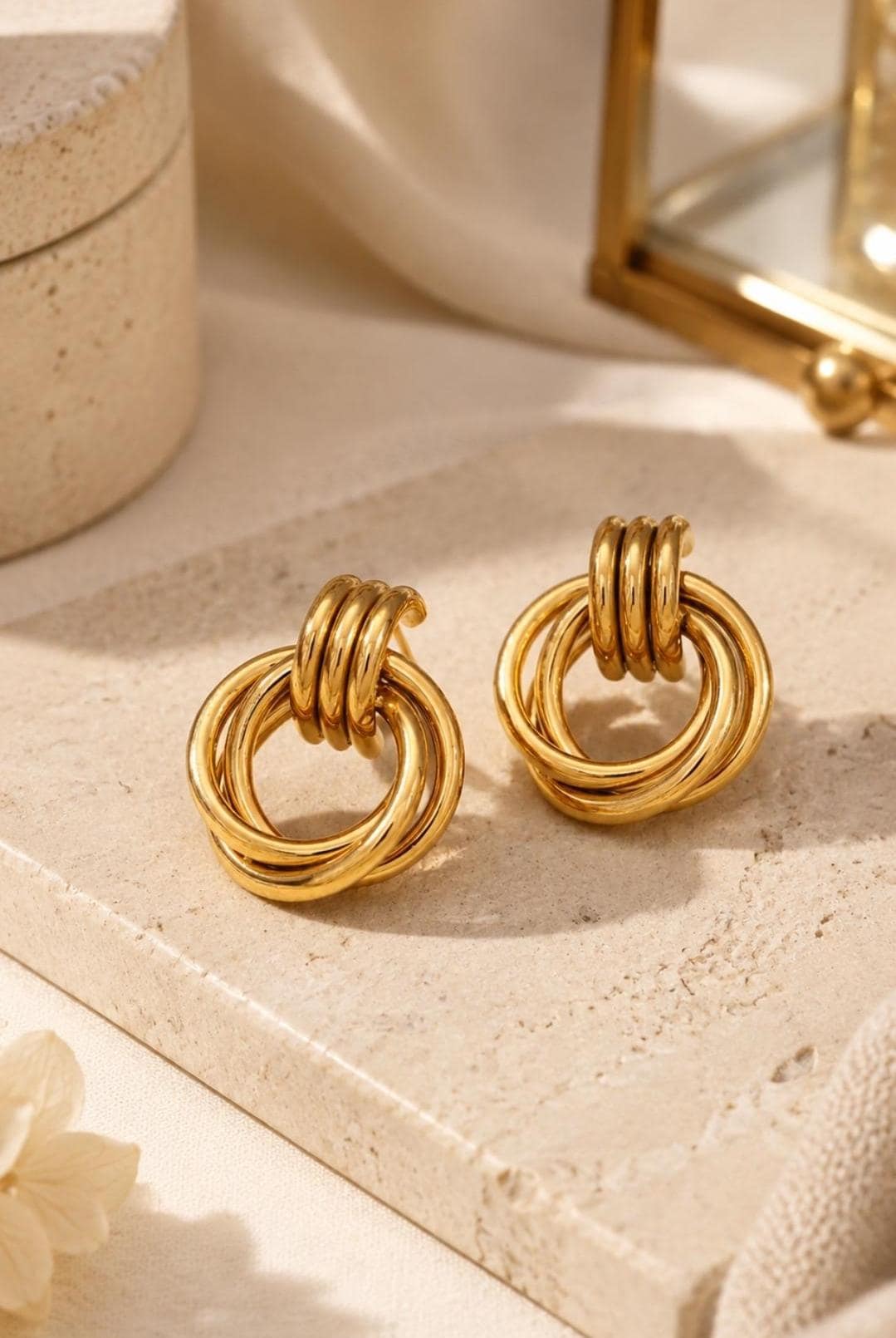 A pair of gold-toned earrings featuring a design of three interlocking circular rings. The earrings have a polished, reflective surface and a post-back closure mechanism, creating a layered, dimensional appearance in a warm metallic finish.