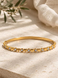 A gold-toned metal bangle bracelet featuring an alternating pattern of small, polished heart shapes and round, clear, sparkling crystals set along the entire outer circumference of the thin, circular band.