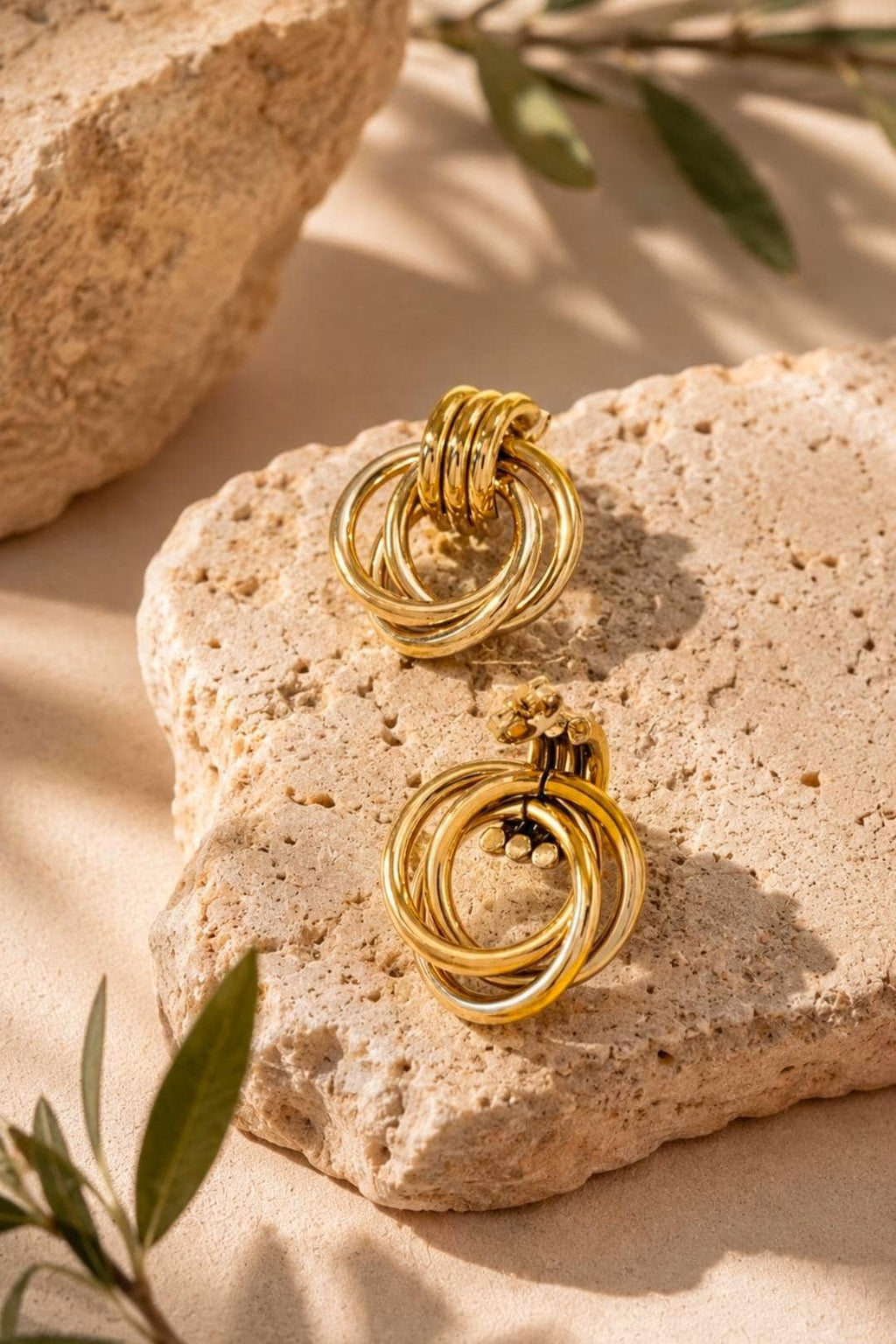 A pair of gold-toned earrings featuring a design of three interlocking circular rings. The earrings have a polished, reflective metallic finish and a post-back closure mechanism visible on the top of each circular structure.