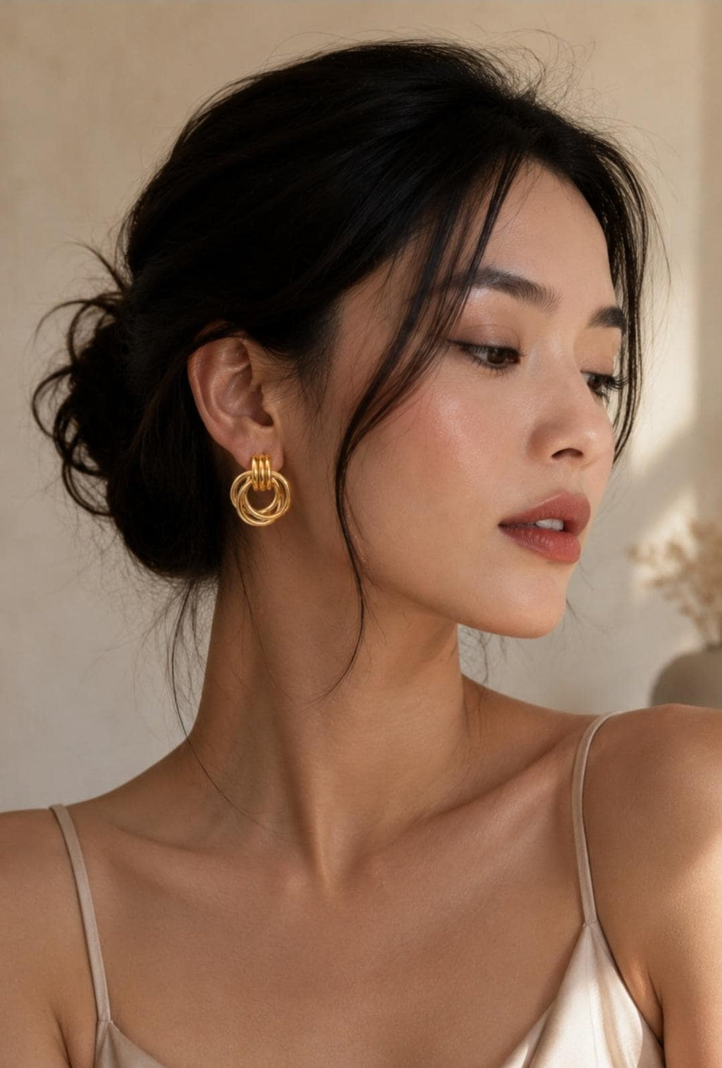 A pair of gold-toned earrings featuring three interlocking circular rings that hang from a small, solid top loop. The earrings have a polished, metallic finish and are worn on the earlobe, complemented by a thin gold-toned chain necklace.