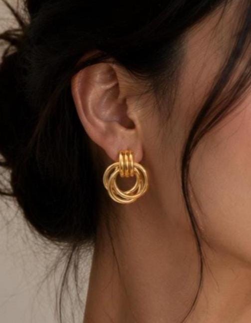 A gold-toned earring featuring a trio of interlocking circular hoops suspended from a small, ribbed cylindrical post. The design consists of three smooth, polished rings that hang freely, creating a layered and dimensional appearance.
